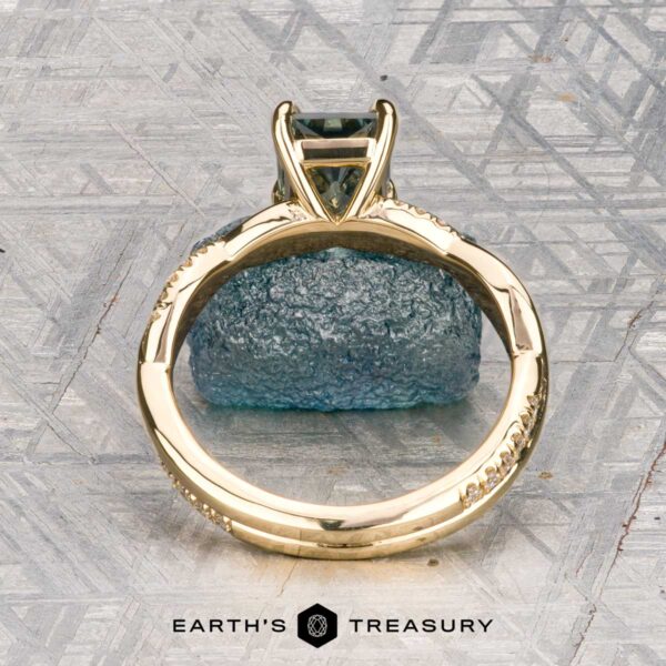 The "Waltz" ring in 18K yellow gold with 1.67-carat Montana sapphire The "Waltz" ring in 18K yellow gold, featuring a 1.67-carat rectangular Montana sapphire and diamond accents, is displayed on a rough blue stone with the "Earth's Treasury" logo beneath.