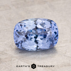 The 2.09-Carat Celyon Sapphire, a faceted, rectangular light blue gemstone with intricate internal reflections, is placed on a textured gray background.