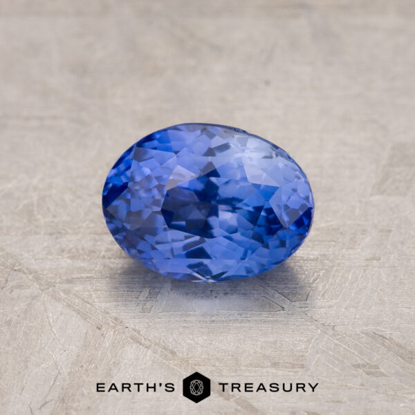 1.52-Carat Celyon Sapphire A close-up image of a 1.52-Carat Violet-Blue Ceylon Sapphire gemstone. The background is a textured, stone-like surface in a neutral color. The text “EARTH’S TREASURY” is visible at the bottom of the image.