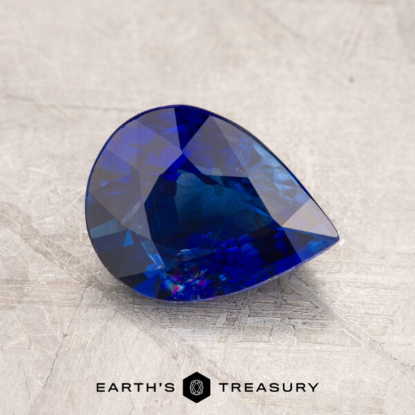 2.01-Carat Deep Royal Blue Ceylon Sapphire (Heated) JM1023L features a pear-shaped, blue gemstone with intricate facets set against a textured gray surface, with the text "Earth's Treasury" displayed at the bottom.