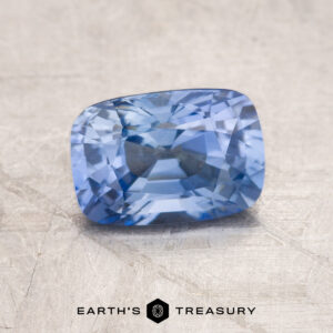 A 1.81-carat rectangular cushion cut blue sapphire is elegantly displayed on a textured surface, with the "Earth's Treasury" logo at the bottom.
