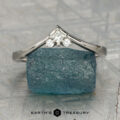A platinum "Sappho" band rests atop a rough blue gemstone, featuring Earth's Treasury branding at the bottom.