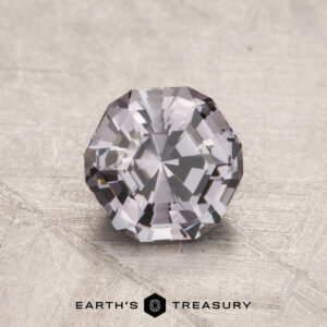 A faceted, clear 1.11-carat Spinel with an octagonal shape rests on a textured surface.