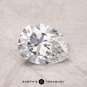 A pear-shaped 1.36-carat diamond with a faceted cut rests on a textured surface.