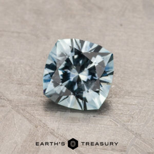 A 2.14-carat Robin's Egg Blue Montana Sapphire (heated) rests on a textured, gray background. The gemstone displays a brilliant mix of light blue hues and intricate facets, capturing light beautifully. The logo "Earth's Treasury" is positioned below the sapphire.