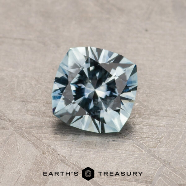 0.88-Carat Montana Sapphire (Heated) A 2.14-carat Robin's Egg Blue Montana Sapphire (heated) rests on a textured, gray background. The gemstone displays a brilliant mix of light blue hues and intricate facets, capturing light beautifully. The logo "Earth's Treasury" is positioned below the sapphire.