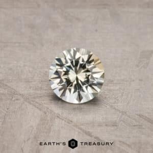 A brilliant-cut round gemstone, the 2.14-Carat Robin’s Egg Blue Montana Sapphire (Heated), displayed on a wooden surface. The gem exhibits a high level of sparkle and clarity. The text "EARTH'S TREASURY" is visible at the bottom of the image.