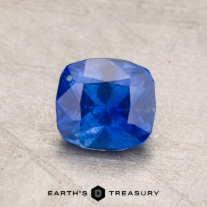 A radiant 2.14-carat Robin's Egg Blue Montana Sapphire, cushion-cut and heated, is showcased against a gray textured background. The bottom center of the image includes the text "EARTH'S TREASURY" with a hexagonal logo between the words.