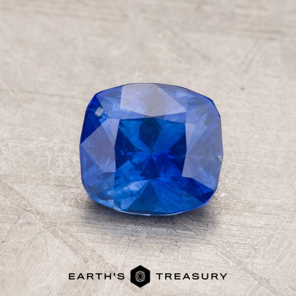 1.41-Carat Sapphire (Heated) A radiant 2.14-carat Robin's Egg Blue Montana Sapphire, cushion-cut and heated, is showcased against a gray textured background. The bottom center of the image includes the text "EARTH'S TREASURY" with a hexagonal logo between the words.