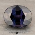 A 3.10-carat bluish violet to purple color-change sapphire, faceted in an oval shape, is showcased against a textured, grey background. The gem's intricate cutting creates a brilliant display of reflective surfaces. Text at the bottom reads "Earth's Treasury.