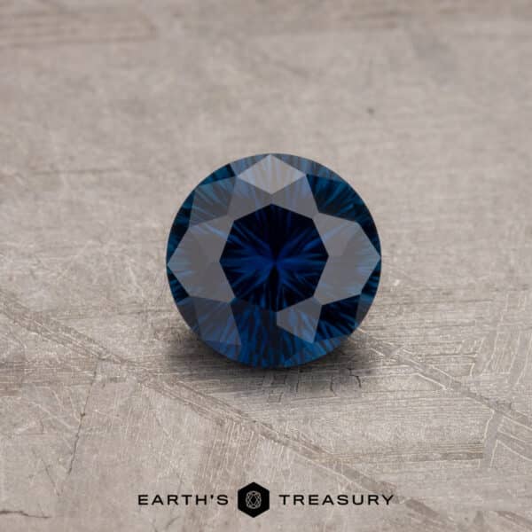 1.06-carat African sapphire A close-up of a round brilliant-cut 1.53-Carat Royal Blue Ceylon Sapphire (Heated) resting on a textured surface. The gemstone has intricate facets, creating a striking star-like pattern when reflecting light. The text "EARTH'S TREASURY" is visible at the bottom of the image.