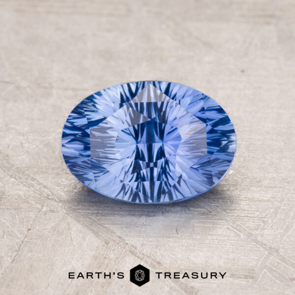 1.82-Carat Ceylon Sapphire A faceted blue 1.82-carat Ceylon Sapphire is displayed on a gray surface, with the text "Earth's Treasury" and its logo visible at the bottom.
