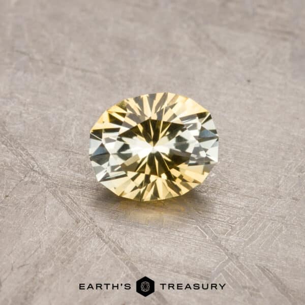 0.97-Carat Montana Sapphire (Heated) A round, faceted 1.53-carat Royal Blue Ceylon Sapphire (heated) is placed on a rough, textured surface. The background features subtle metallic tones. The logo "EARTH'S TREASURY" and a hexagonal emblem are visible at the bottom.