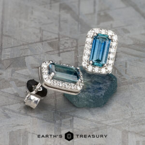 The EA-MS-510 earrings feature rectangular Montana Sapphires with diamond halos, set in silver and displayed on a textured gray surface with the Earth's Treasury logo at the bottom.