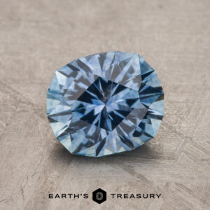 A 1.89-carat Sky Blue Montana Sapphire (Heated) with a starburst pattern rests on a textured gray surface above the text "Earth's Treasury.