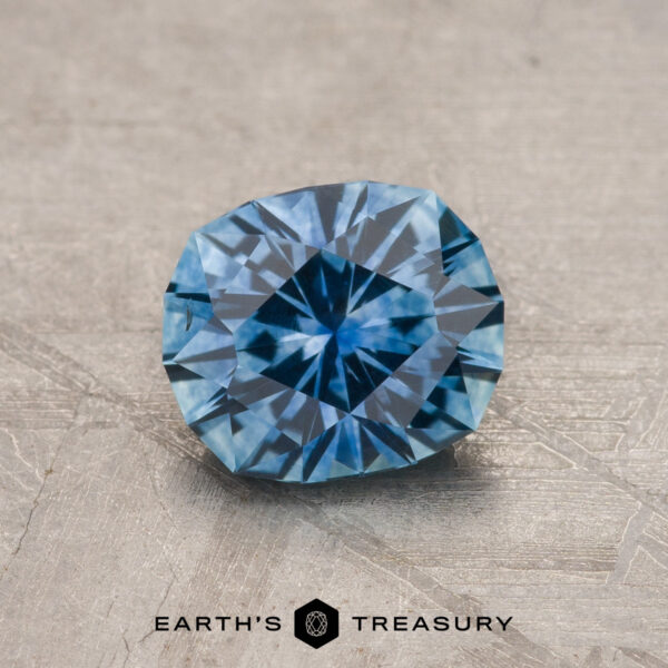 1.27-Carat Medium Blue Montana Sapphire (Heated) A 1.27-carat medium blue Montana Sapphire (heated) is displayed on a textured surface with "Earth's Treasury" text and logo below.