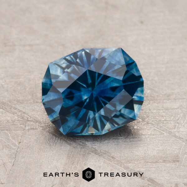 1.52-Carat Peacock Blue Montana Sapphire (Heated) A faceted 1.52-Carat Peacock Blue Montana Sapphire (Heated) is shown on a light textured surface, with the "Earth's Treasury" text and logo beneath it.