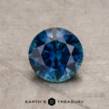 A 1.21-Carat Deep Peacock Blue Montana Sapphire (Heated), round brilliant-cut, rests on a textured surface with the "Earth's Treasury" logo and text displayed at the bottom of the image.