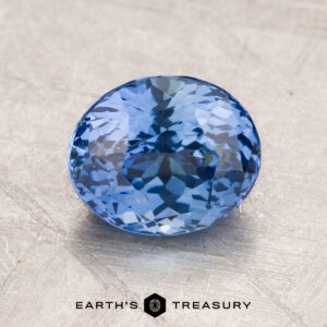 Close-up image of a faceted oval-blue 2.34-Carat Sapphire displayed on a textured surface, with the text "Earth's Treasury" below it.
