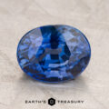 A 5.21-Carat Sapphire, expertly cut in an oval shape, is showcased on a light textured surface with the "Earth's Treasury" logo and text displayed below.