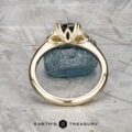 The "Lillium" ring in 14k yellow gold with a 1.38-carat Australian sapphire, accented by two clear stones and shown on a rough blue crystal, with the Earth's Treasury logo beneath.