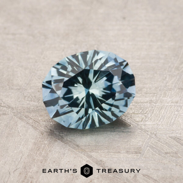 1.17-Carat Aqua Blue Montana Sapphire (Heated) A 1.17-carat aqua blue Montana sapphire (heated), oval faceted, rests on a textured surface with "EARTH'S TREASURY" displayed at the bottom.