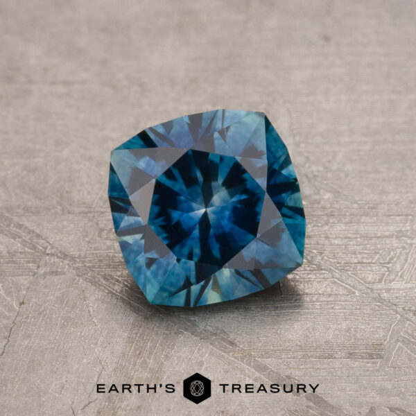 1.13-Carat Peacock Blue Montana Sapphire (Heated) A 1.13-Carat Peacock Blue Montana Sapphire (Heated), cushion-cut, sits on a textured gray surface with the "Earth's Treasury" logo and text beneath it.