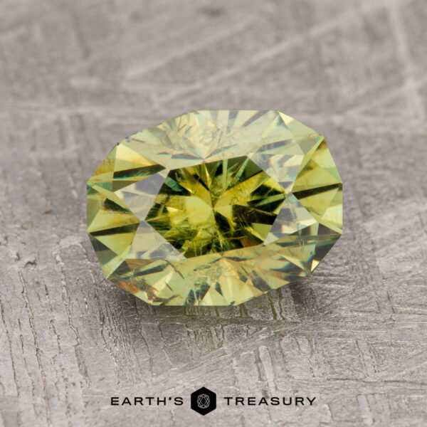 2.43-Carat Olive Green Demantoid Garnet A 2.43-carat olive green demantoid garnet is displayed on a textured gray surface with the text "EARTH'S TREASURY" below.