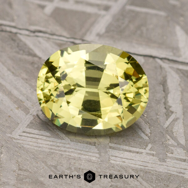 1.78-Carat Greenish-Yellow Mali Garnet A faceted, oval-cut 1.78-carat Mali Garnet, placed on a textured gray surface, with the logo and text "Earth's Treasury" visible at the bottom.