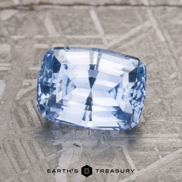 A stunning 2.79-carat light blue Ceylon sapphire (heated) with a detailed cut is placed on a textured surface. The logo "Earth's Treasury" is prominently visible below the gemstone.