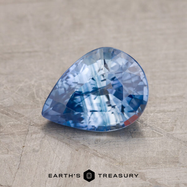1.50-Carat Sky-Pale Blue Particolored Ceylon Sapphire (Heated) A 1.50-carat, pear-shaped, faceted Ceylon sapphire (heated) is placed on a textured surface with the text "Earth's Treasury" visible at the bottom of the image.