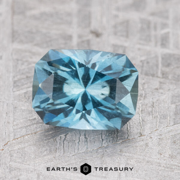 1.39-Carat Nasarawa Teal Aqua A faceted blue gemstone with a radiant cut placed on a textured background. Text below reads "1.39-Carat Nasarawa Teal Aqua by Earth's Treasury.