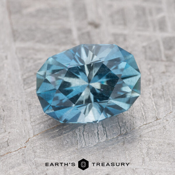 1.45-Carat Nasarawa Teal Aqua A faceted, oval blue gemstone resting on a textured gray surface, with the text "1.45-Carat Nasarawa Teal Aqua" at the bottom.