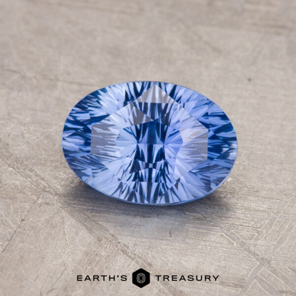 1.82-Carat Rich Sky Blue Ceylon Sapphire A faceted blue 1.82-carat Ceylon Sapphire is displayed on a gray surface, with the text "Earth's Treasury" and its logo visible at the bottom.
