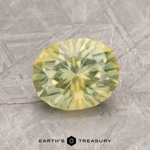2.11-Carat Yellow-Green Particolored Montana Sapphire A faceted yellow 2.11-Carat Montana Sapphire displayed on a textured surface with the words "Earth's Treasury" beneath it.