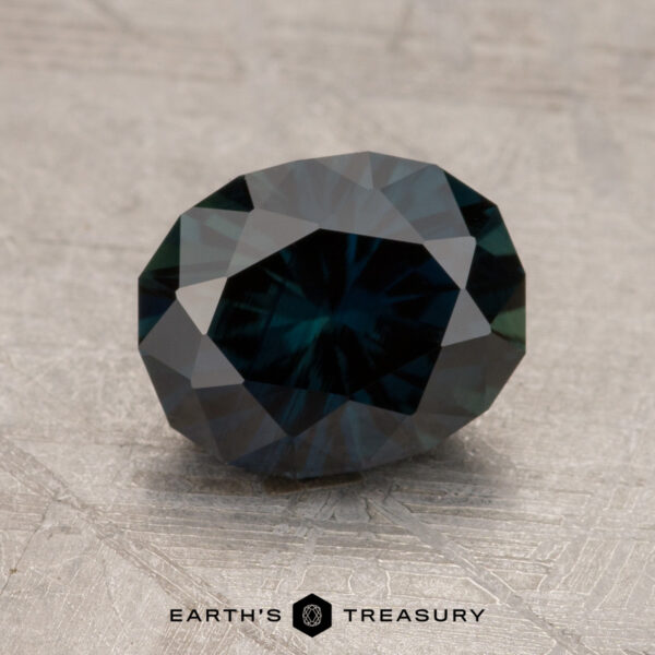 2.17-Carat Near Black Australian Sapphire (Heated) A polished 2.17-Carat Australian Sapphire with facets reflecting light, set on a textured surface. The text "Earth's Treasury" is underneath the gemstone.