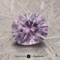A close-up of a 2.34-carat pale gray-lavender to pink-purple color change Umba Sapphire on a textured surface. The text "Earth's Treasury" appears at the bottom of the image.