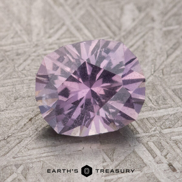 2.34-Carat Pale Gray-Lavender to Pink-Purple Color Change Umba Sapphire A close-up of a 2.34-carat pale gray-lavender to pink-purple color change Umba Sapphire on a textured surface. The text "Earth's Treasury" appears at the bottom of the image.