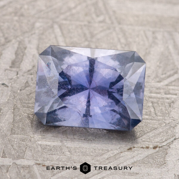 2.14-Carat Violet Umba Sapphire A 2.14-carat violet Umba sapphire, cut in a rectangular shape, sits on a textured surface. The gemstone features a symmetrical internal pattern and is labeled "Earth's Treasury" at the bottom.
