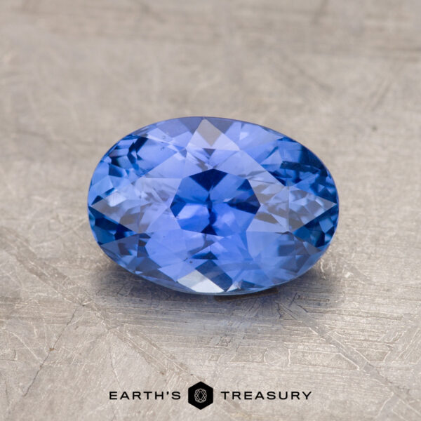 1.83-Carat Violet-Blue Ceylon Sapphire A 1.83-carat oval-cut Ceylon sapphire, featuring intricate facets, is showcased against a textured background. Text at the bottom center of the image reads "EARTH'S TREASURY.