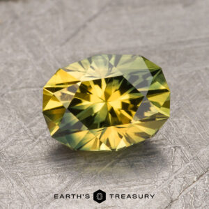 A 2.28-carat Australian sapphire, featuring a faceted yellow-green hue with intricate cuts, rests on a textured metallic surface. The text "Earth's Treasury" is visible below the gemstone.
