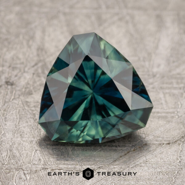 2.44-Carat Deep Blue-Green Australian Sapphire (Heated) A faceted, trilliant-cut 2.44-carat Australian sapphire gemstone positioned on a textured surface. The stone is displayed with the logo "Earth's Treasury" beneath it.
