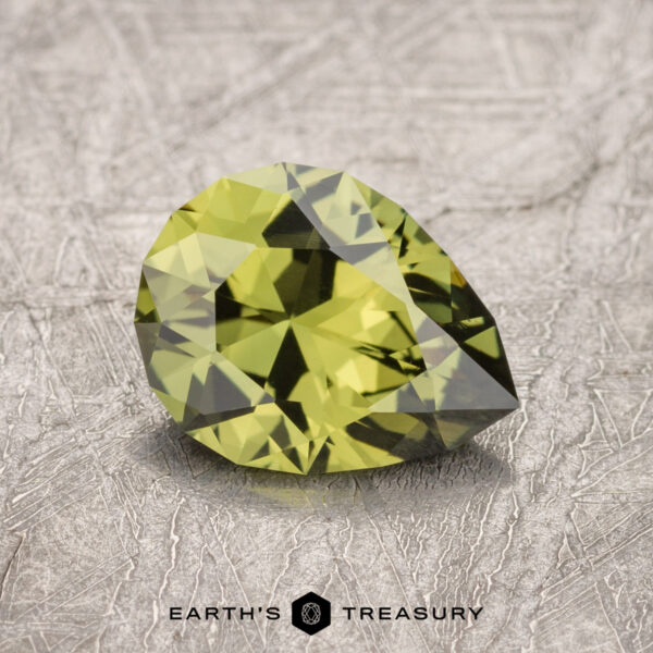 1.47-Carat Olive Green Australian Sapphire (Heated) A 1.47-carat Australian sapphire, displaying a stunning faceted yellow-green hue, rests on a textured surface with the text "EARTH'S TREASURY" below it.
