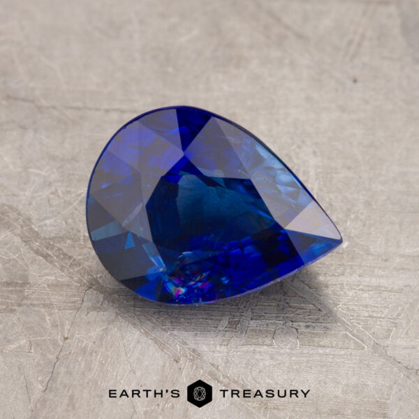 2.01-Carat Deep Royal Blue Ceylon Sapphire (Heated) JM1023L features a pear-shaped, blue gemstone with intricate facets set against a textured gray surface, with the text "Earth's Treasury" displayed at the bottom.