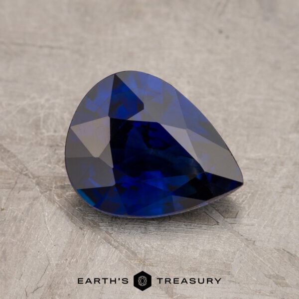 1.74-Carat Deep Royal Blue Ceylon Sapphire (Heated) A faceted blue JM1026L gemstone on a textured surface with the "Earth's Treasury" logo at the bottom.