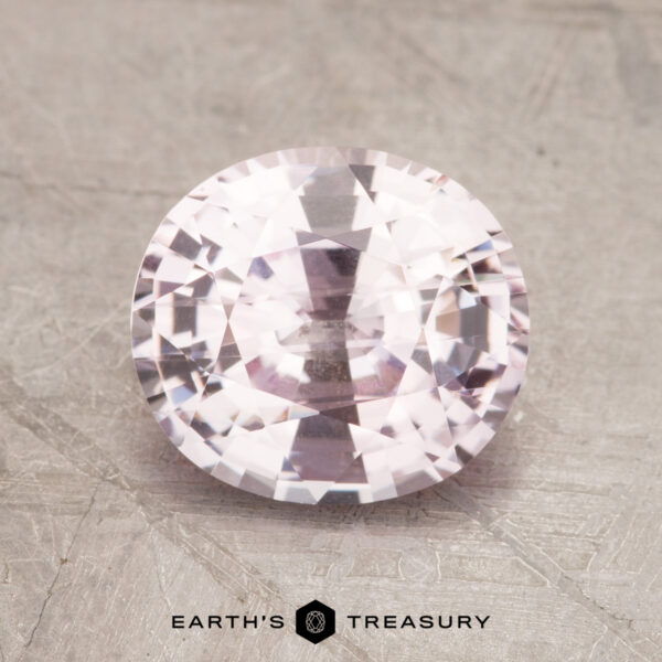 2.31-Carat Pale Pink Sapphire A 2.31-carat faceted, oval-cut light pink sapphire displayed on a textured gray surface with the "EARTH'S TREASURY" logo beneath it.