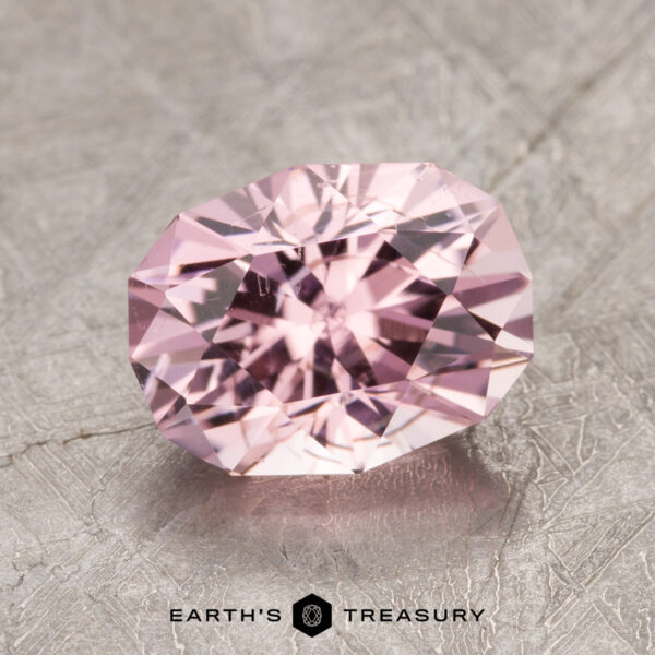 2.01-Carat Pink Tourmaline An ET1614 gemstone with a faceted pink oval cut resting on a textured metallic surface bears the label "EARTH'S TREASURY.