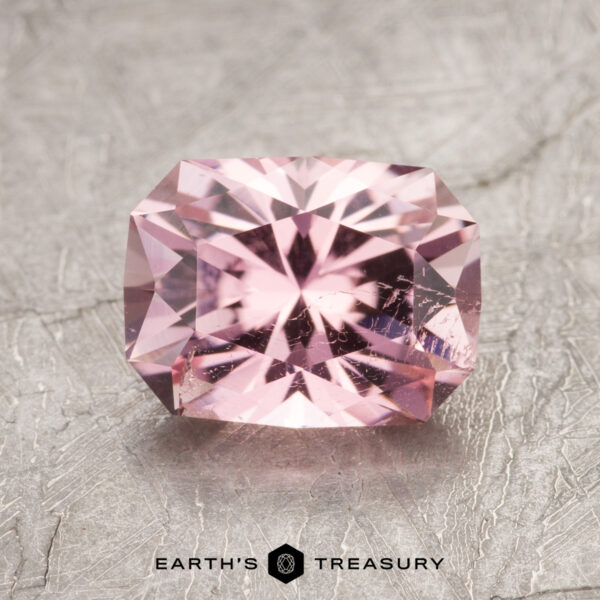 A rectangular pink gemstone with brilliant facets placed on a textured grey surface. Text at the bottom reads "ET1625 Earth's Treasury.