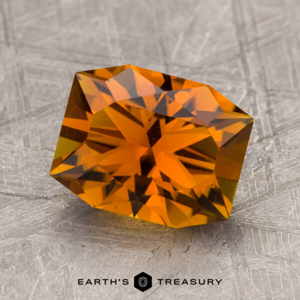 2.37-Carat Autumn Orange Tourmaline A faceted orange 2.37-carat tourmaline lies on a textured gray surface. The bottom part of the image features the text "Earth's Treasury.