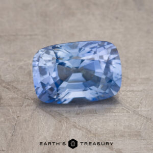 A 1.81-carat rectangular cushion cut blue sapphire is elegantly displayed on a textured surface, with the "Earth's Treasury" logo at the bottom.